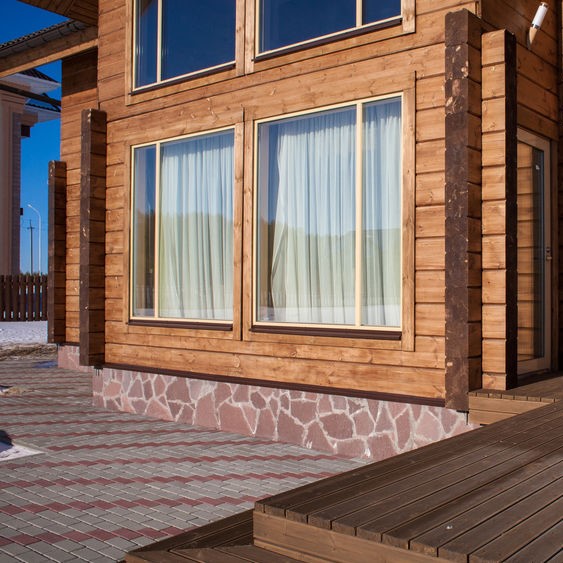 Fachada de vivienda de madera con ventanas y terraza de tablón exterior.